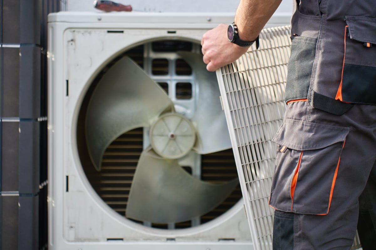 Technician removing the front cover from an outdoor heat pump unit during a service call