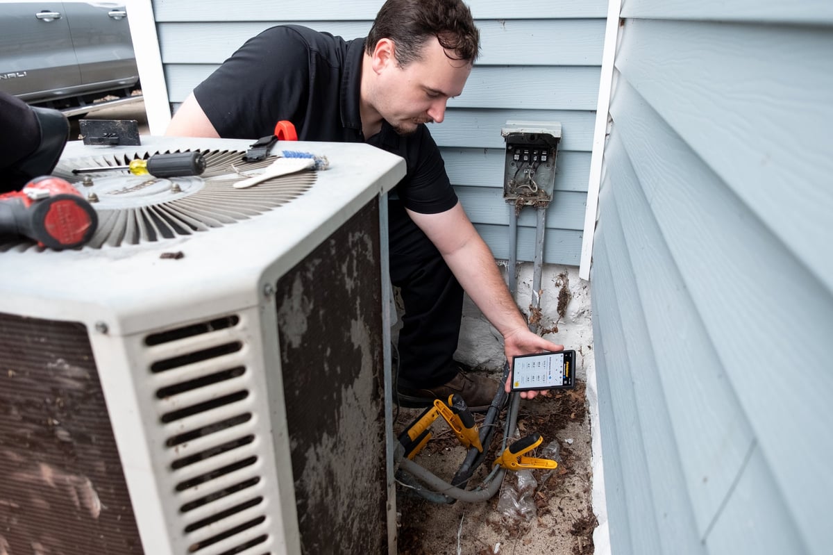 HVAC technician servicing an outdoor air conditioning unit with tools and electrical equipment visible